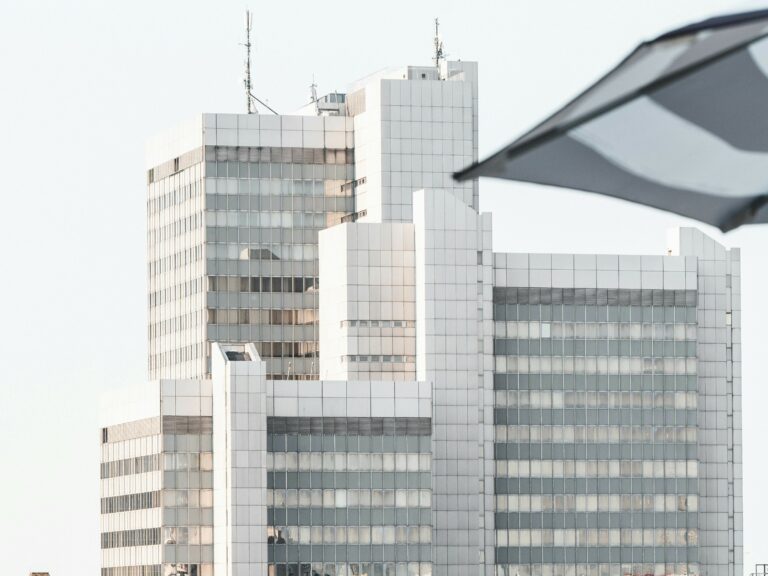 Das Stadthaus Bonn an einem klaren Tag. Im Vordergrund ist ein Teil eines Schirms, der das Gebäude teilweise überdeckt. Dies symbolisiert den Tarifvertrag für den öffentlichen Dienst (TVöD).