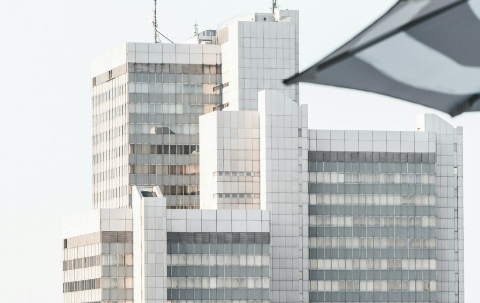 Das Stadthaus Bonn an einem klaren Tag. Im Vordergrund ist ein Teil eines Schirms, der das Gebäude teilweise überdeckt. Dies symbolisiert den Tarifvertrag für den öffentlichen Dienst (TVöD).