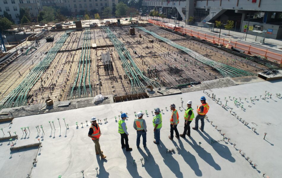 Mehrere Bauarbeiter sind auf einer großen Baustelle zu sehen, die anscheinend eine Besprechung durchführen. SOKA-Bau steht im Zusammenhang mit der Sozialkasse der Bauwirtschaft, die für die Absicherung von Urlaub, Ausbildung und Rentenbeiträgen in der Baubranche zuständig ist. Unternehmen im Baugewerbe müssen Beiträge an die SOKA-Bau leisten, um sicherzustellen, dass die Mitarbeiter auch während Phasen der Arbeitsunterbrechung sozial abgesichert sind.