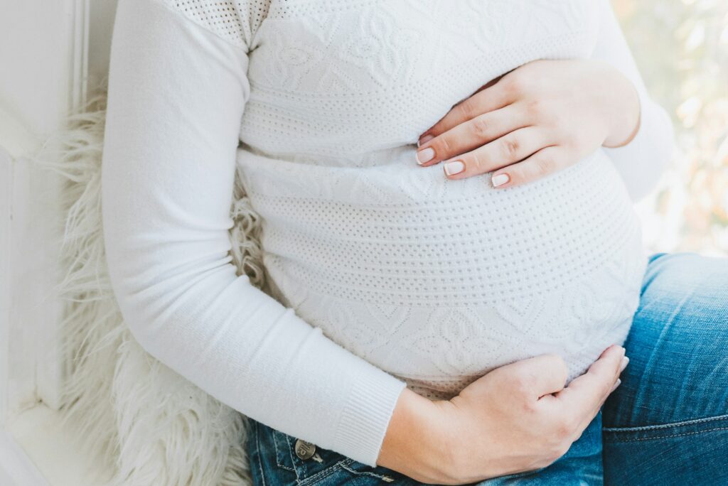 Eine schwangere Person, die ihren Bauch mit beiden Händen hält und entspannte, positive Ausstrahlung vermittelt. Der Fokus liegt auf der Schwangerschaft, was symbolisch für Mutterschutz und die damit verbundenen Regelungen steht. Es verweist auf die Schutzmaßnahmen für Schwangere am Arbeitsplatz, die durch ein Beschäftigungsverbot geregelt werden, um Gesundheit und Sicherheit von Mutter und Kind zu gewährleisten.