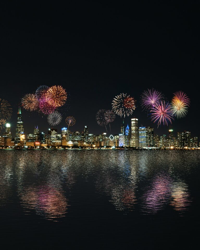 Ein nächtlicher Stadtblick zeigt eine beleuchtete Skyline mit buntem Feuerwerk am Himmel, das sich im ruhigen Wasser darunter spiegelt. Die Szene strahlt Feierlichkeit, Reflexion und einen Neuanfang aus, der mit einem festlichen Ereignis verbunden ist. Jahresabschluss verweist hier auf den feierlichen Abschluss eines erfolgreichen Geschäftsjahres, das Gelegenheit bietet, Erfolge zu feiern, Rückschau zu halten und mit neuem Elan in das kommende Jahr zu starten.