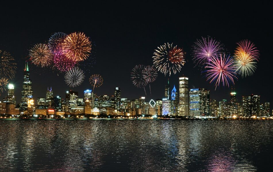 Ein nächtlicher Stadtblick zeigt eine beleuchtete Skyline mit buntem Feuerwerk am Himmel, das sich im ruhigen Wasser darunter spiegelt. Die Szene strahlt Feierlichkeit, Reflexion und einen Neuanfang aus, der mit einem festlichen Ereignis verbunden ist. Jahresabschluss verweist hier auf den feierlichen Abschluss eines erfolgreichen Geschäftsjahres, das Gelegenheit bietet, Erfolge zu feiern, Rückschau zu halten und mit neuem Elan in das kommende Jahr zu starten.