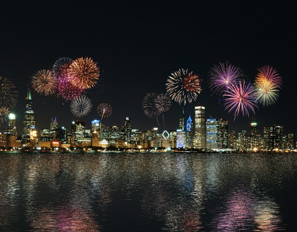 Ein nächtlicher Stadtblick zeigt eine beleuchtete Skyline mit buntem Feuerwerk am Himmel, das sich im ruhigen Wasser darunter spiegelt. Die Szene strahlt Feierlichkeit, Reflexion und einen Neuanfang aus, der mit einem festlichen Ereignis verbunden ist. Jahresabschluss verweist hier auf den feierlichen Abschluss eines erfolgreichen Geschäftsjahres, das Gelegenheit bietet, Erfolge zu feiern, Rückschau zu halten und mit neuem Elan in das kommende Jahr zu starten.