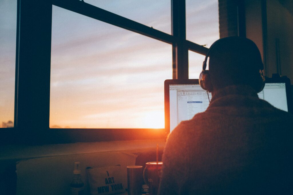 Das Bild zeigt eine Person, die am Computer arbeitet, während die Sonne untergeht. Dies kann symbolisieren, dass auch bei längerer Krankheit die Lohnfortzahlung durch den Arbeitgeber sichergestellt werden muss. Die Lohn- und Gehaltsabrechnung spielt hierbei eine zentrale Rolle, um die gesetzlichen Ansprüche korrekt umzusetzen.